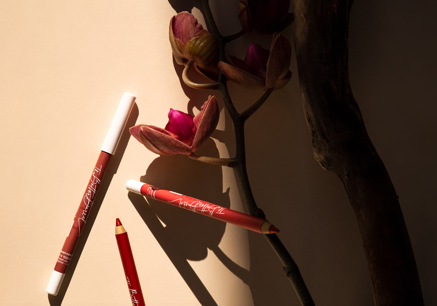 Styled product photo of red make-up liners placed next to a branch and a flower.